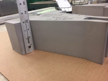 Close-up of a 4” thick 304H stainless steel part with a ruler for scale, produced by Sandmeyer Steel Company using a waterjet machining center for an industrial pipe support system.