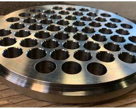 Two images of a machined stainless steel tubesheet made from 316/316L dual-certified material. The tubesheet features a machined beveled edge, raised face, and 55 precision-drilled holes with a diameter tolerance of +.002/-.004. The part was plasma cut and finished with machining to meet exacting customer specifications, with a 12.250” OD and .875” thickness.