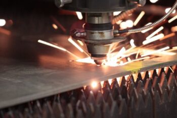 Laser cutting stainless steel plate with sparks visible at the cutting point.